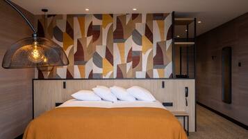A hotel room with a bed, a large wall art piece, a hanging lamp, and a wooden floor.