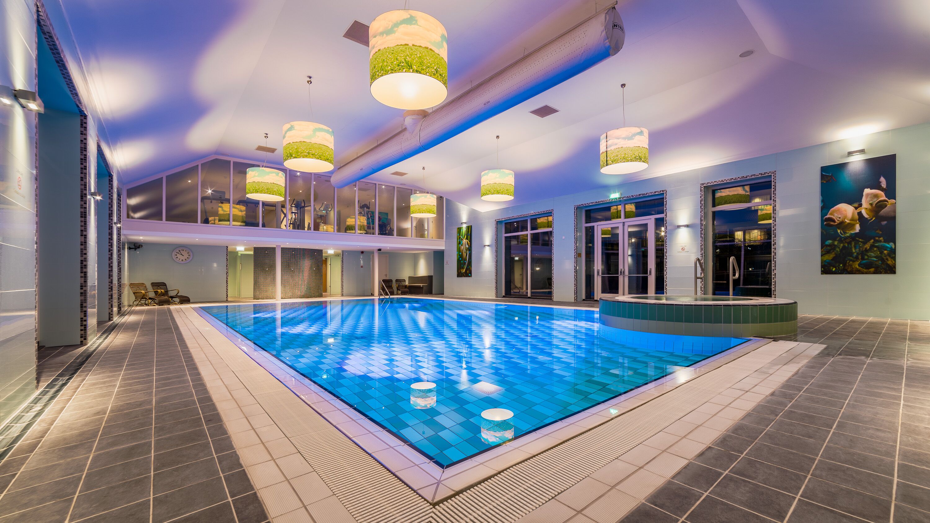 An indoor swimming pool with a tiled floor, ceiling lights, and a glass door entrance.