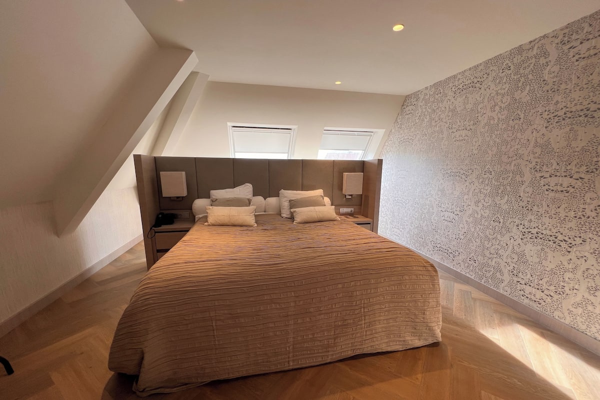 A modern bedroom with a large bed, wooden headboard, and a sloped ceiling.