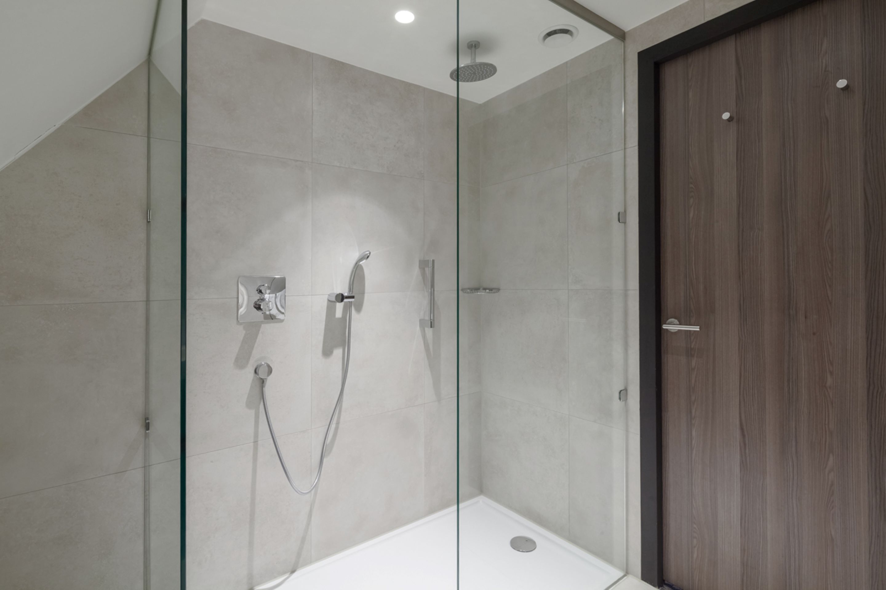 A modern shower area with a glass partition, a wooden door, and a tiled floor.