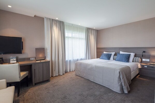 A modern hotel room with a large bed, a desk, and a TV.