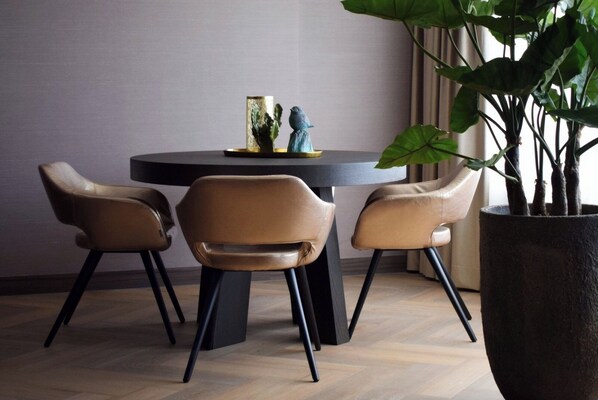 Un coin repas avec une table ronde, trois fauteuils en cuir et une plante en pot.