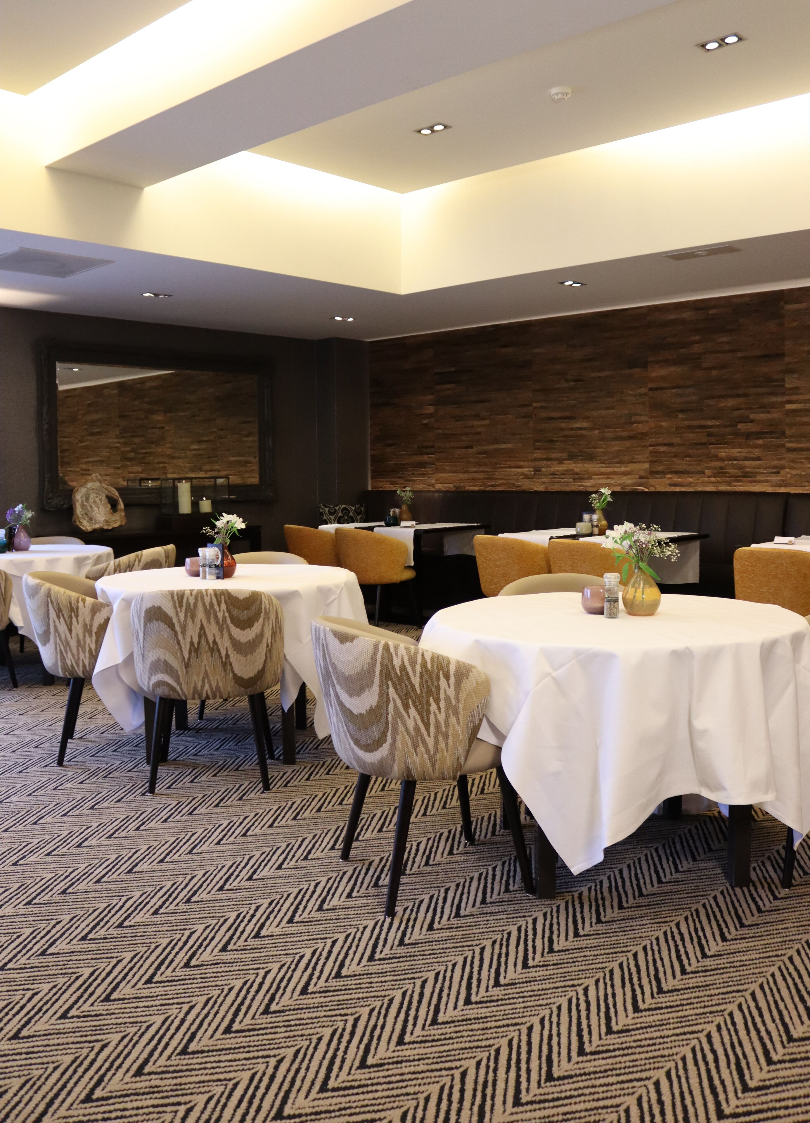 Ein Essbereich eines Hotels mit runden Tischen, Stühlen und einem gemusterten Teppich.