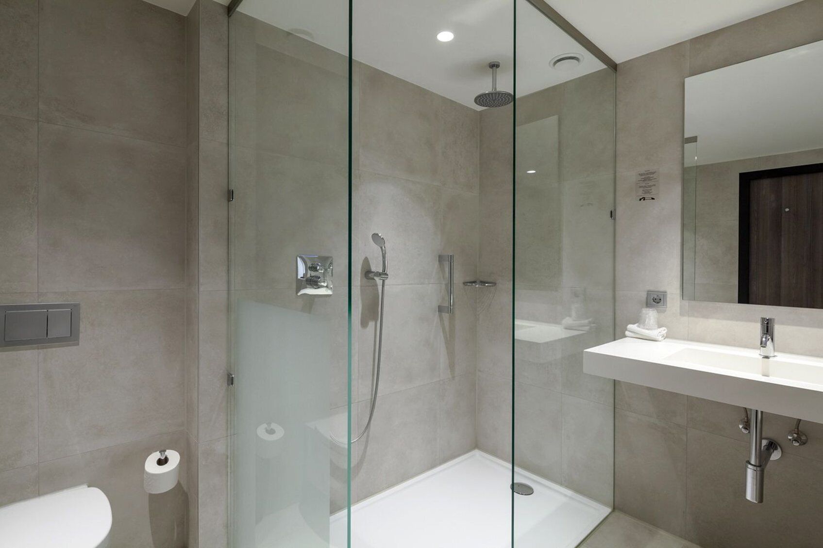 Ein modernes Badezimmer mit einer gläsernen Duschkabine, einem weißen Waschbecken und einem großen Spiegel.