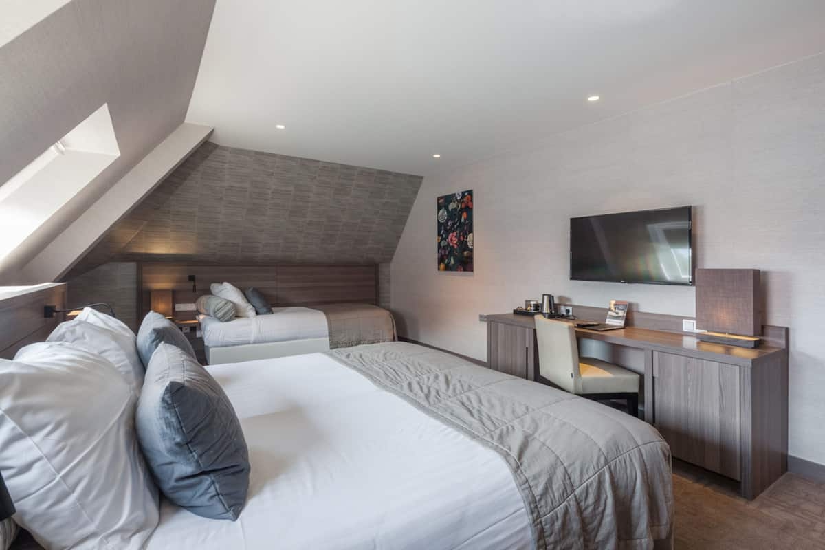 A modern hotel room with two beds, a desk, and a TV.