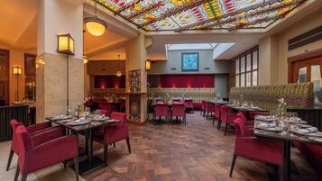 Een restaurant met rode stoelen, houten tafels en een plafond van glas-in-lood.