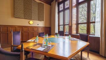 Un salón de conferencias con una amplia mesa de madera, varias sillas y un gran ventanal con vidrieras.