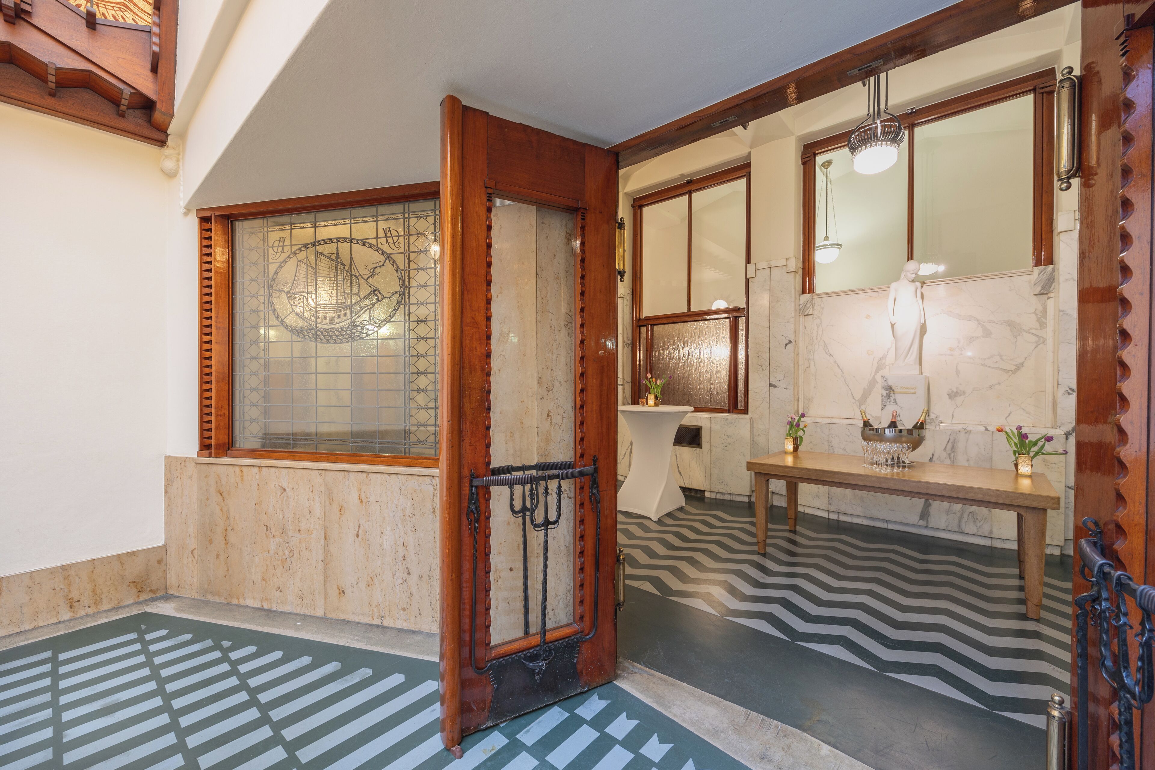 Um hall com porta de madeira, piso de azulejos, balcão de recepção de mármore e um espelho grande.