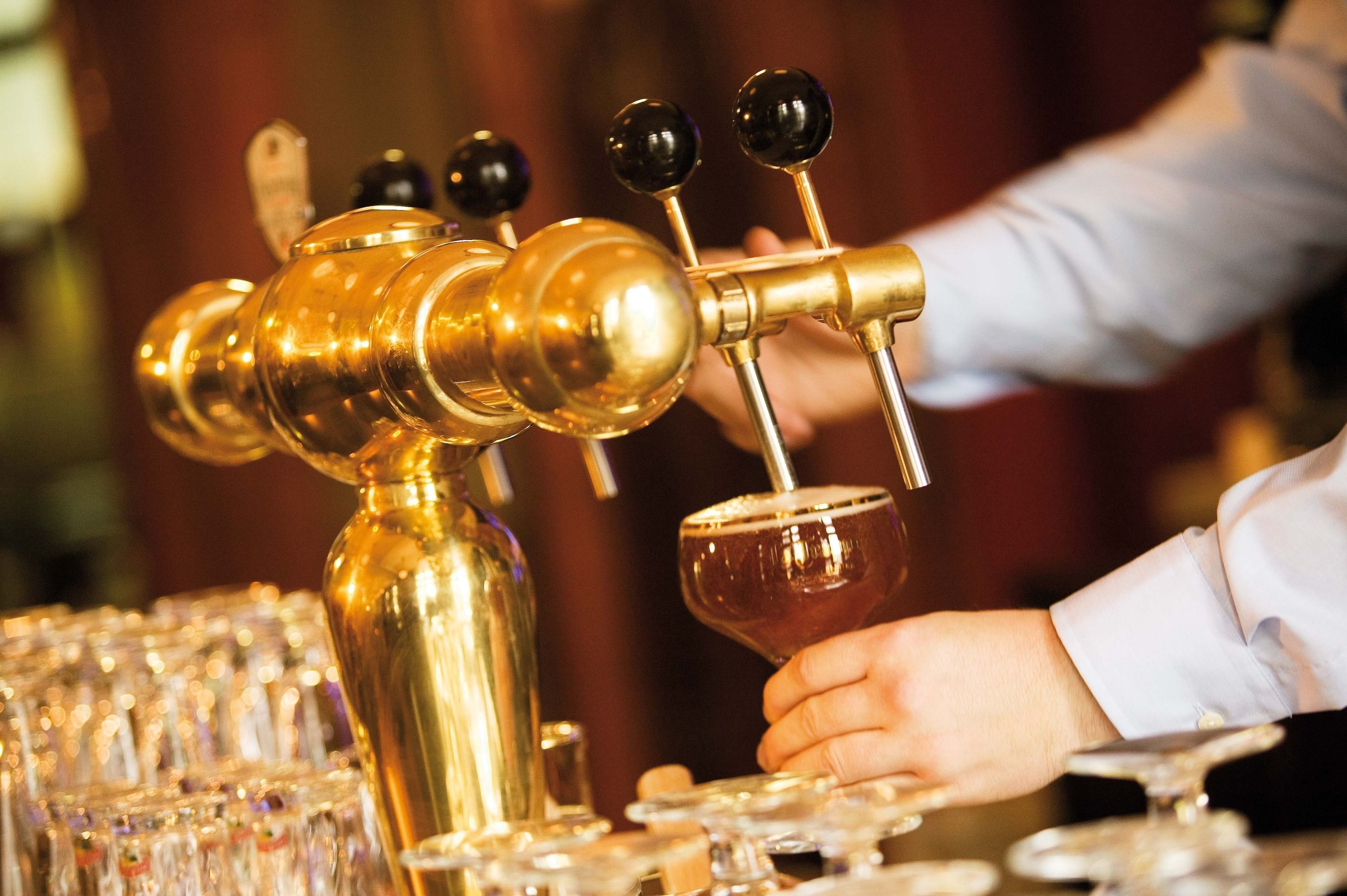 Um bartender servindo uma bebida de uma torneira dourada para um copo.