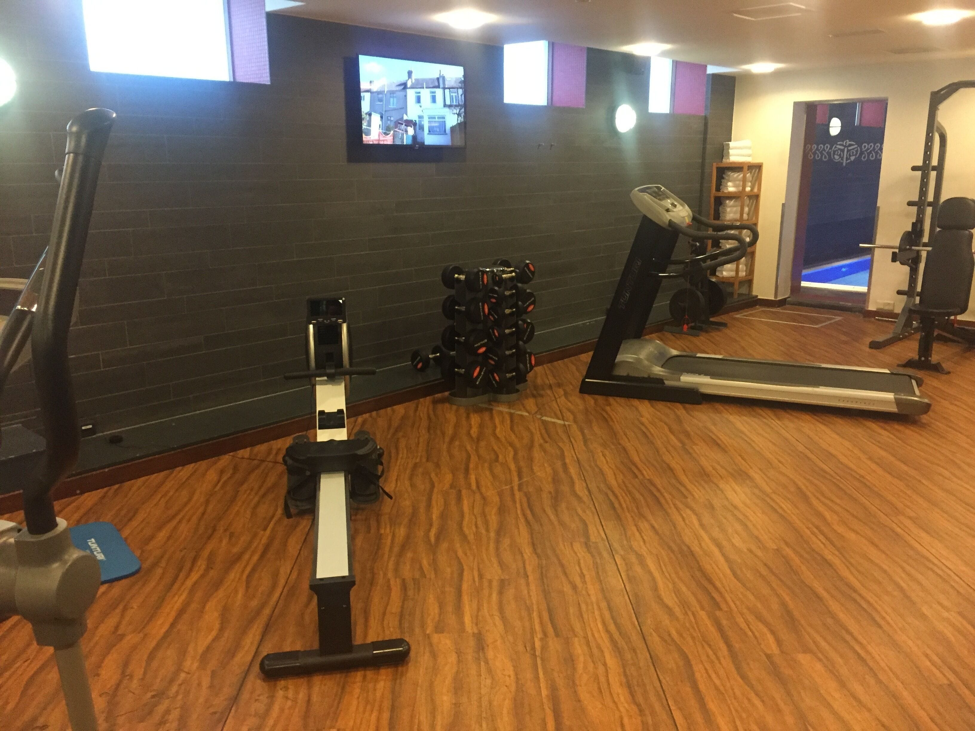 Une salle de sport équipée de matériel d’exercice, avec un téléviseur accroché au mur et un plancher en bois.