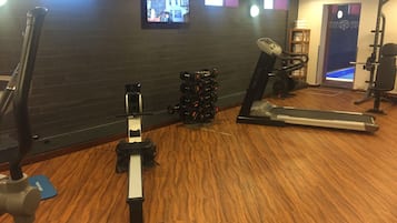 Une salle de sport équipée de matériel d’exercice, avec un téléviseur accroché au mur et un plancher en bois.