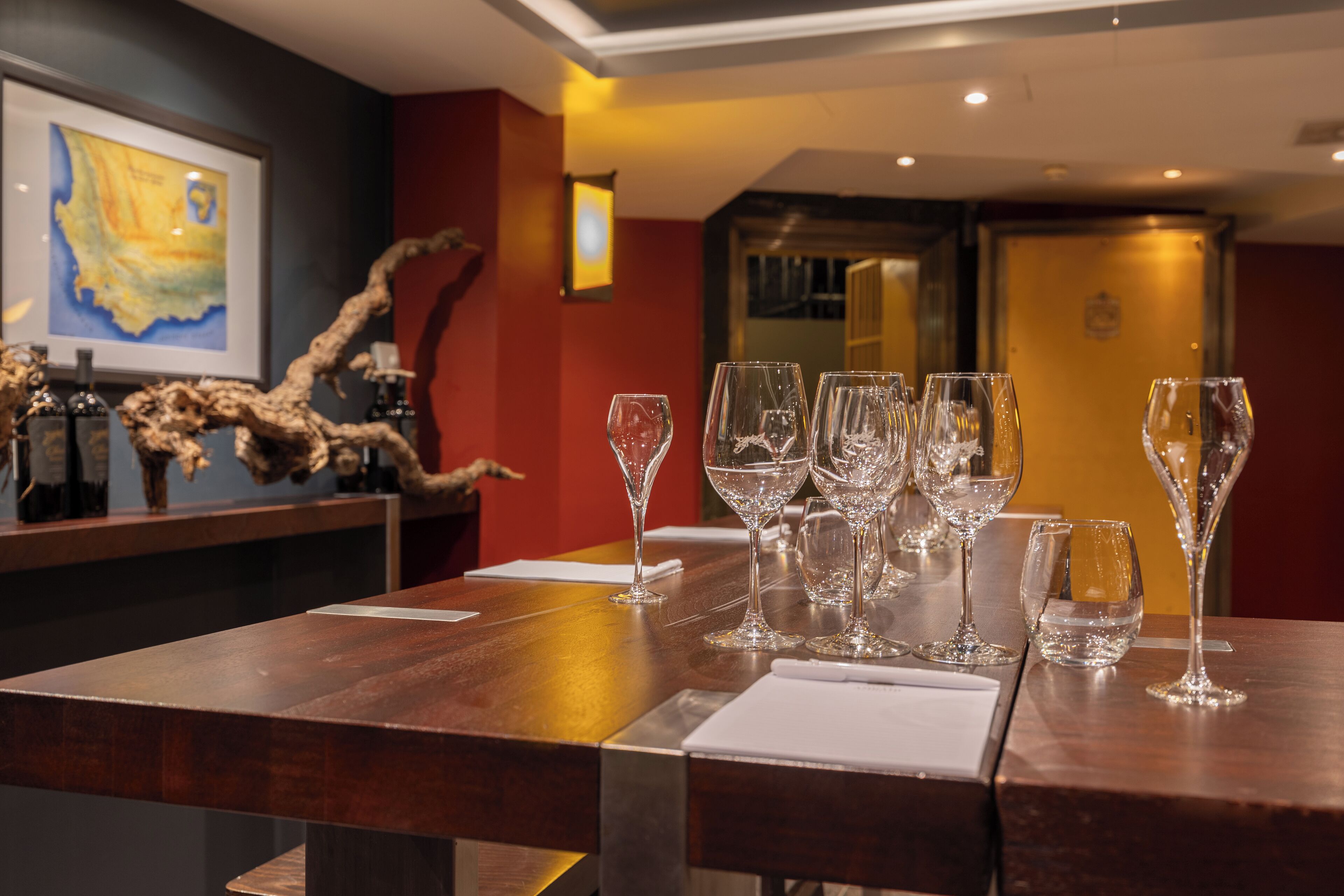 A bar area with multiple wine glasses and bottles, a framed map on the wall, and a wooden counter.