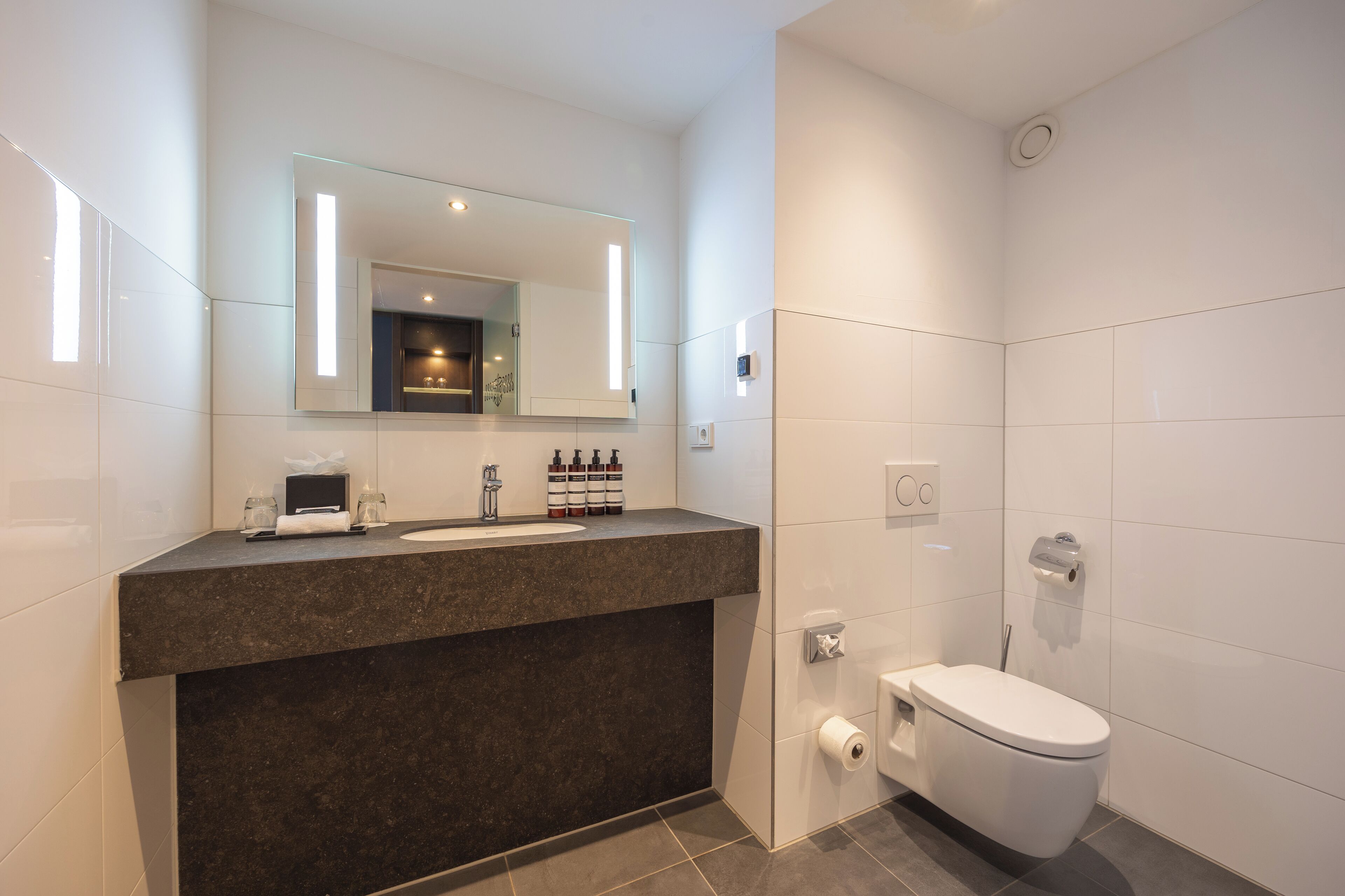 A modern bathroom with a dark granite countertop, a large mirror, and a white toilet.