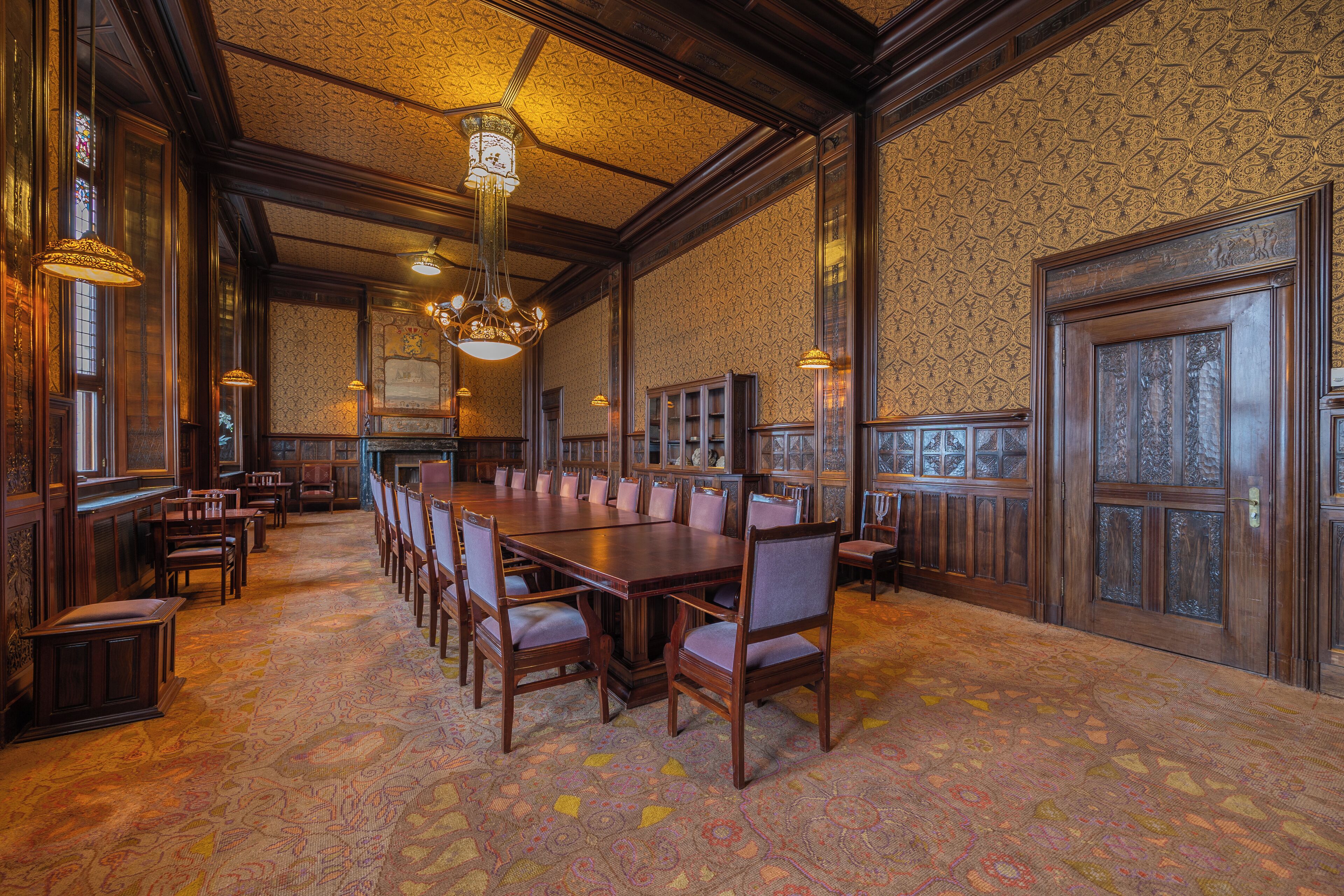 A large conference room with a long wooden table, multiple chairs, and ornate chandeliers.