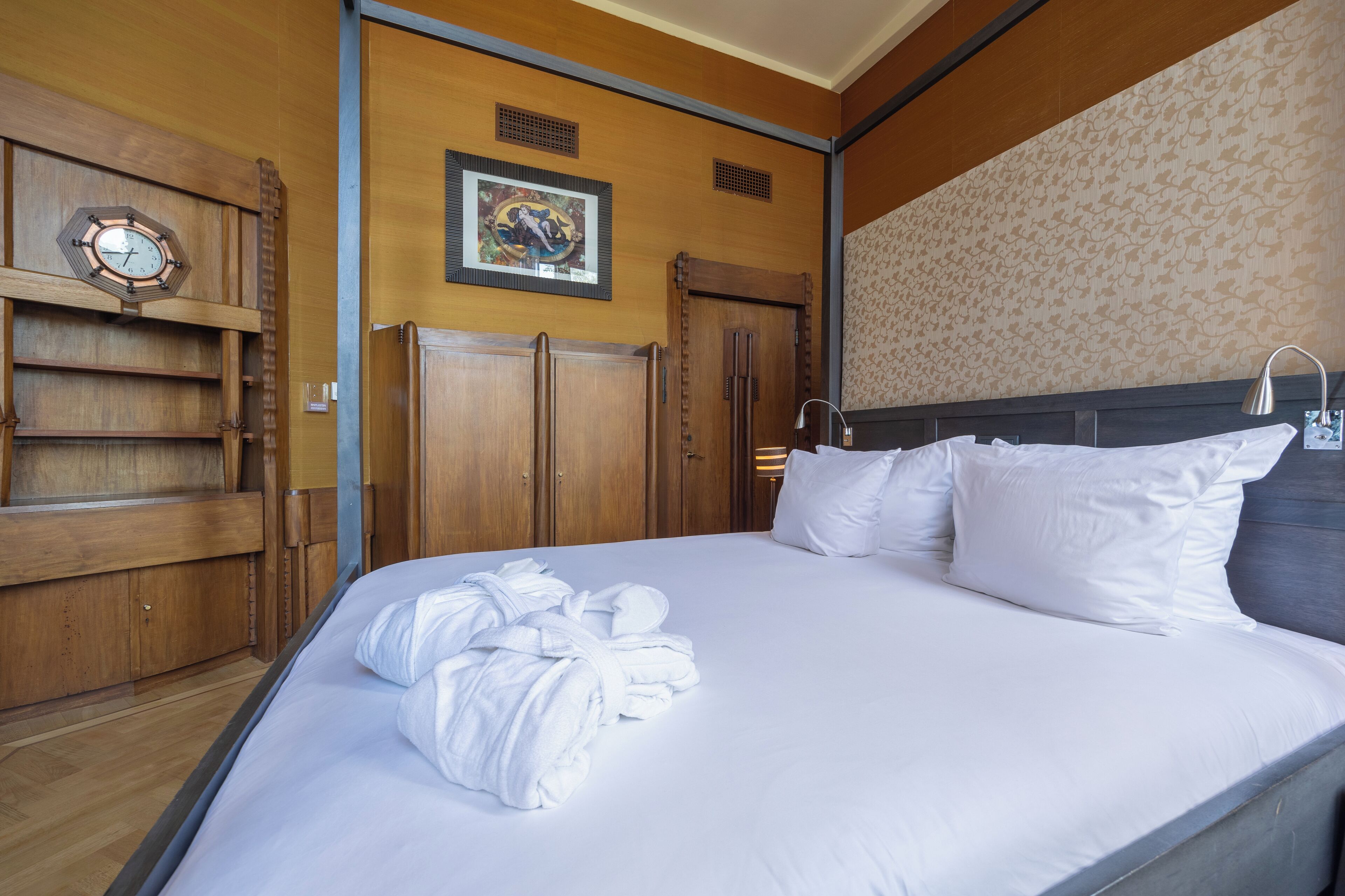 A neatly made bed with white linens and a pile of white bathrobes on the left side.