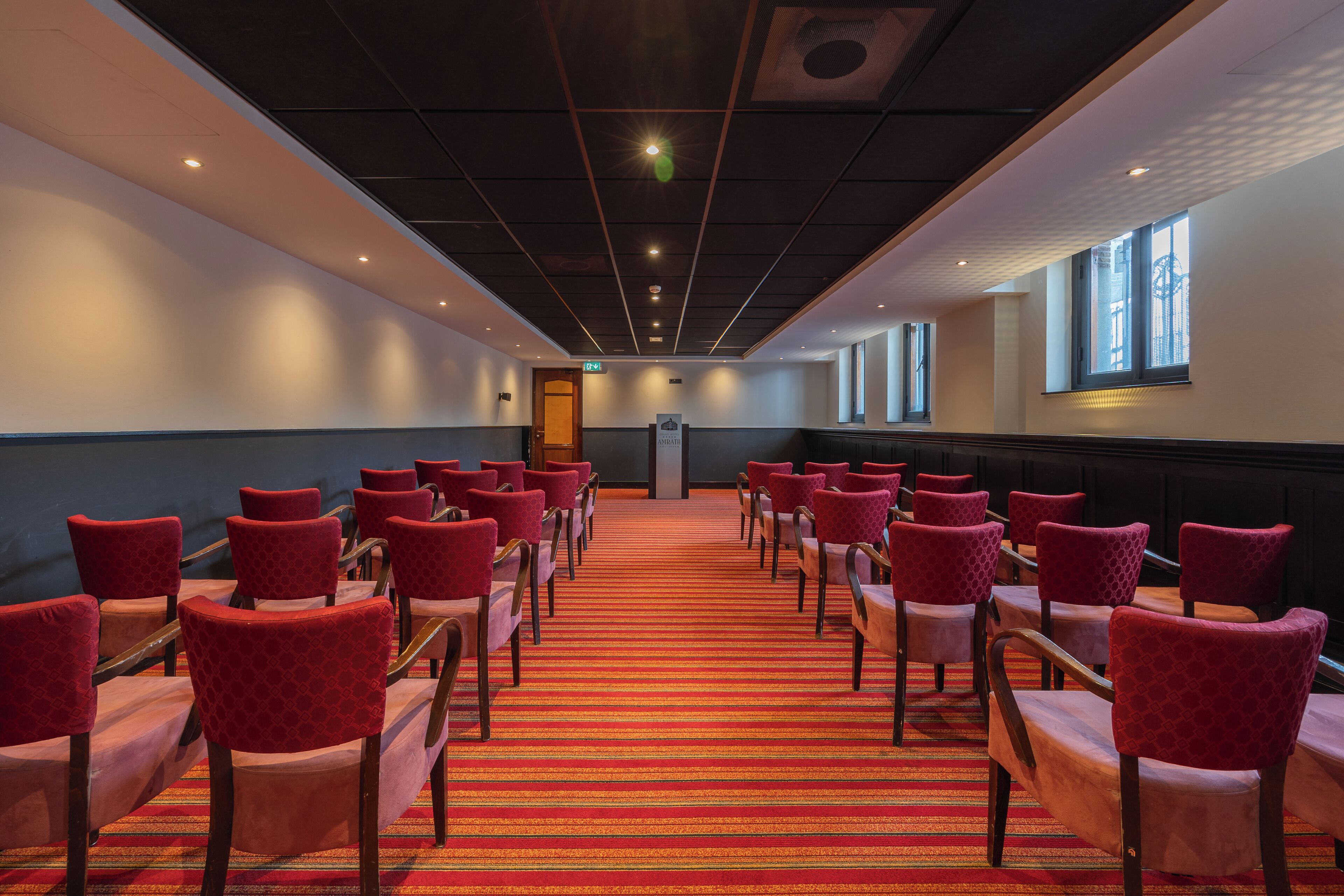 A conference room with rows of red chairs and a red carpet.