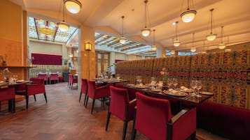 A restaurant with wooden flooring, red upholstered chairs, and hanging pendant lights.