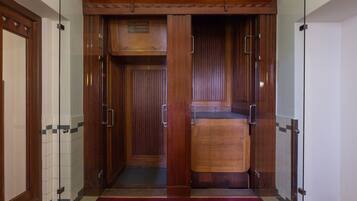 An elevator with wooden doors and a metal handle, leading to a room with a tiled floor and a red carpet.