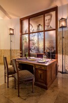 Un bureau en bois avec un séparateur en verre, deux chaises, une lampe et une petite table sur laquelle se trouvent une carafe et des verres.
