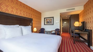 Habitación de hotel con una cama grande, dos sillones, una mesita, un escritorio con silla, televisión y un cuadro en la pared.