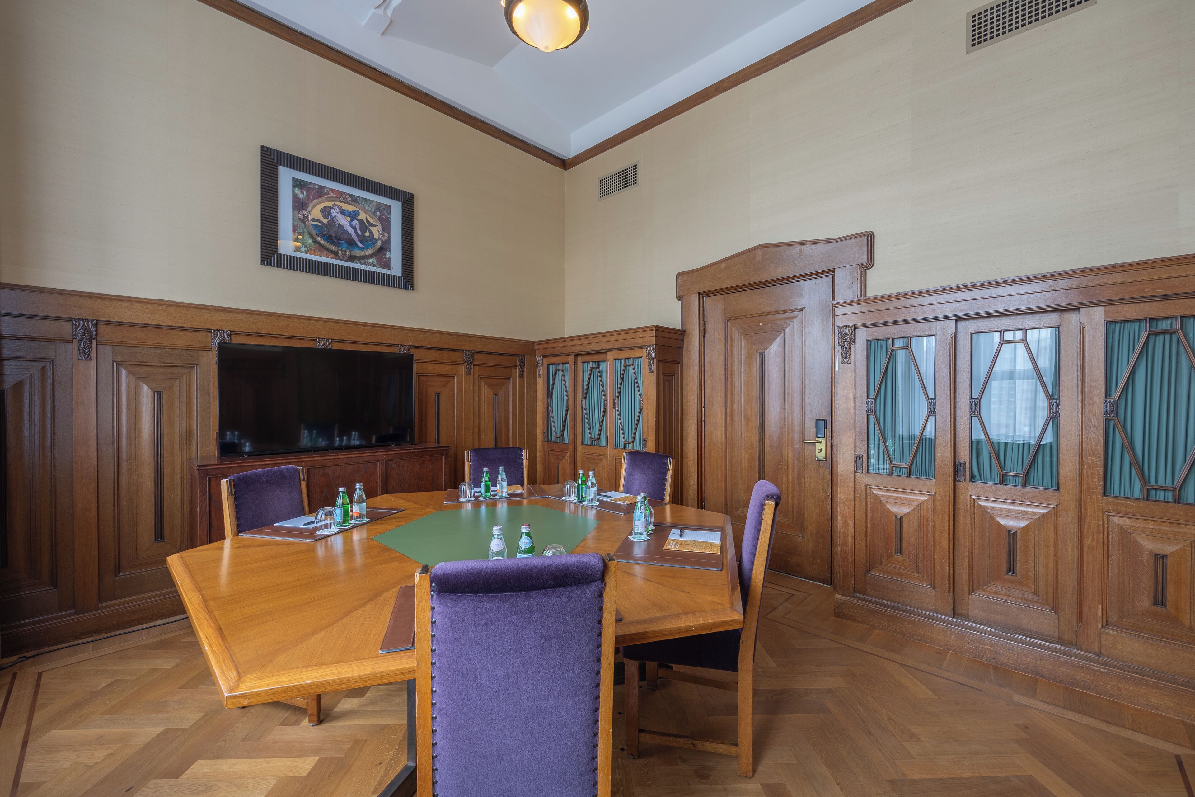A conference room with a large wooden table, chairs, a television, and a framed picture on the wall.