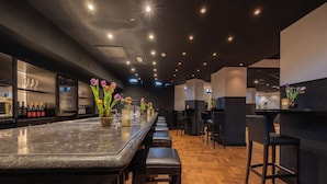 Uma área de bar moderna com um balcão extenso, vários bancos e uma variedade de garrafas e copos.