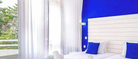 Habitación de hotel con una cama grande, ropa de cama blanca y azul, una pared de acento azul y cortinas translúcidas.