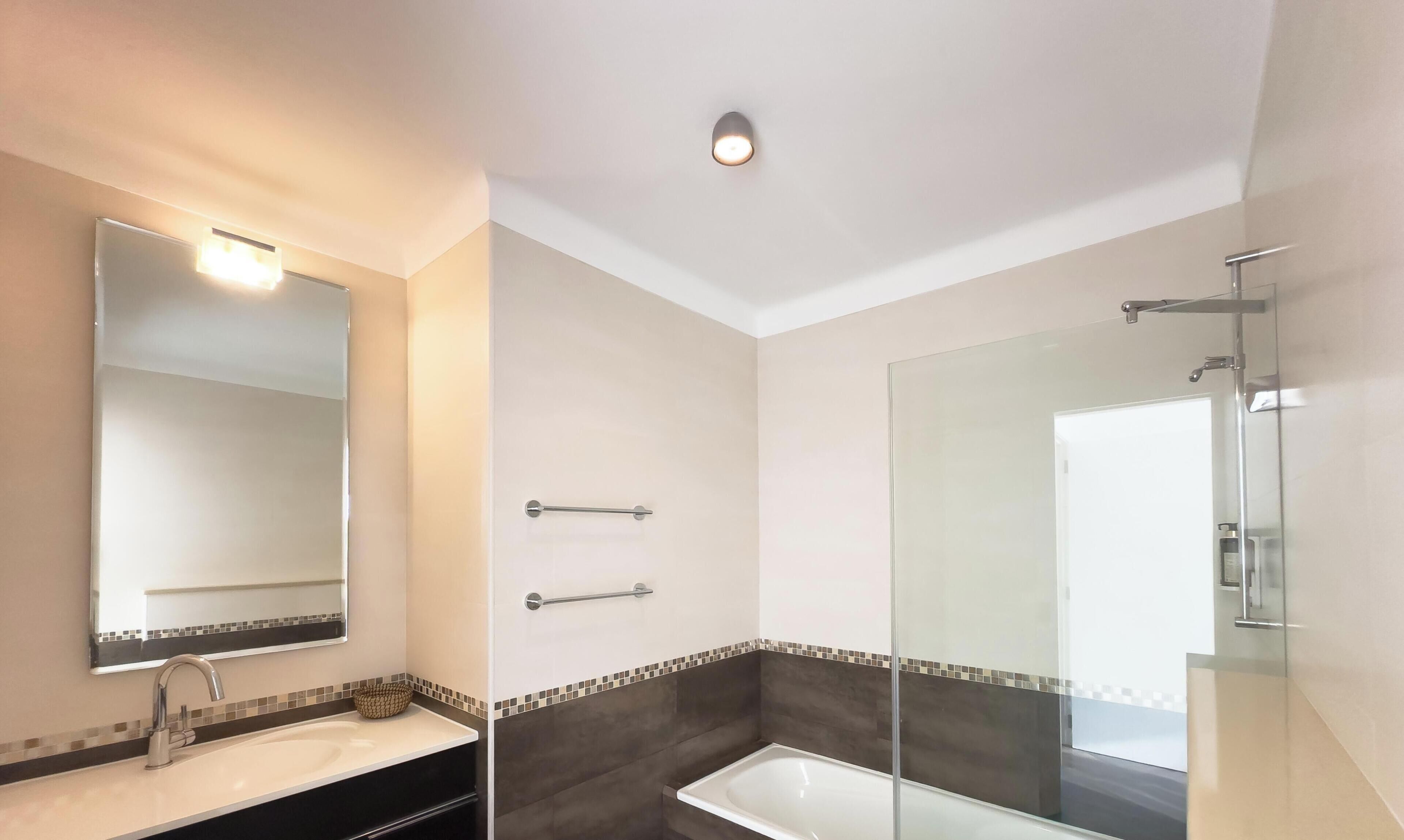 Une salle de bain moderne avec un grand miroir, un lavabo, une baignoire et une douche.