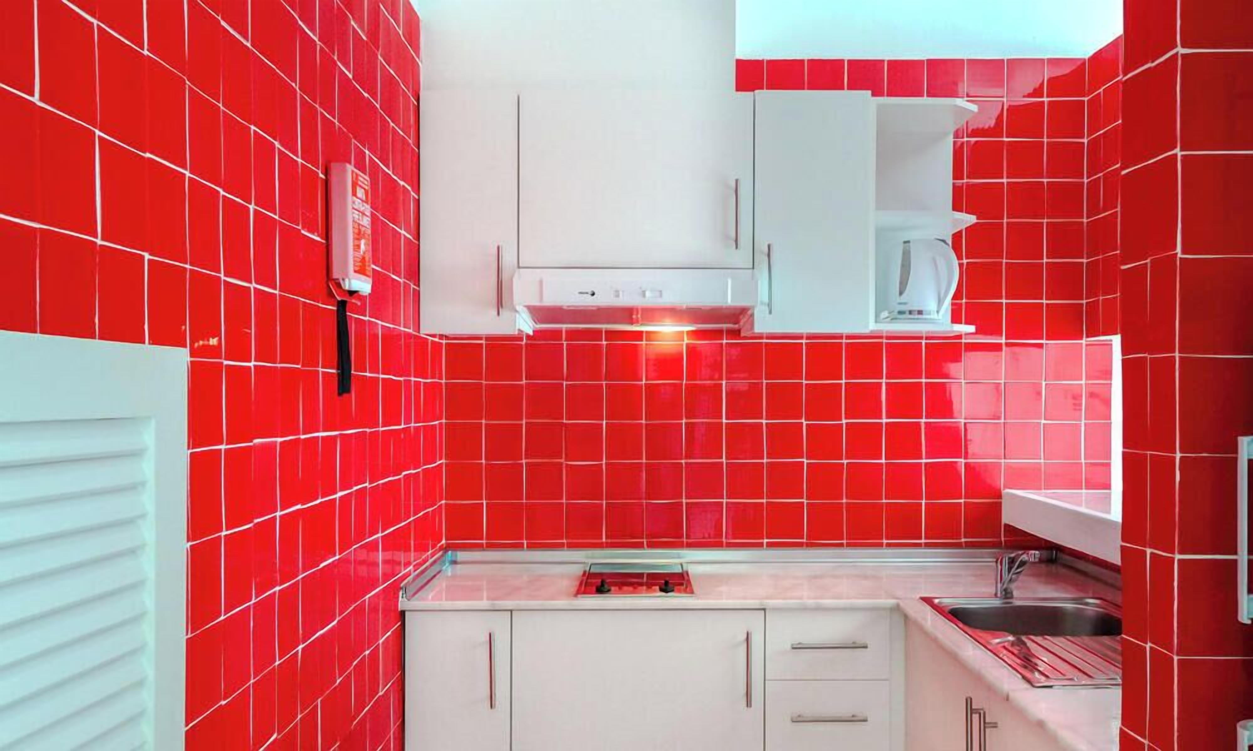 Una cucina con piastrelle rosse, mobili bianchi e un lavello in acciaio inossidabile.