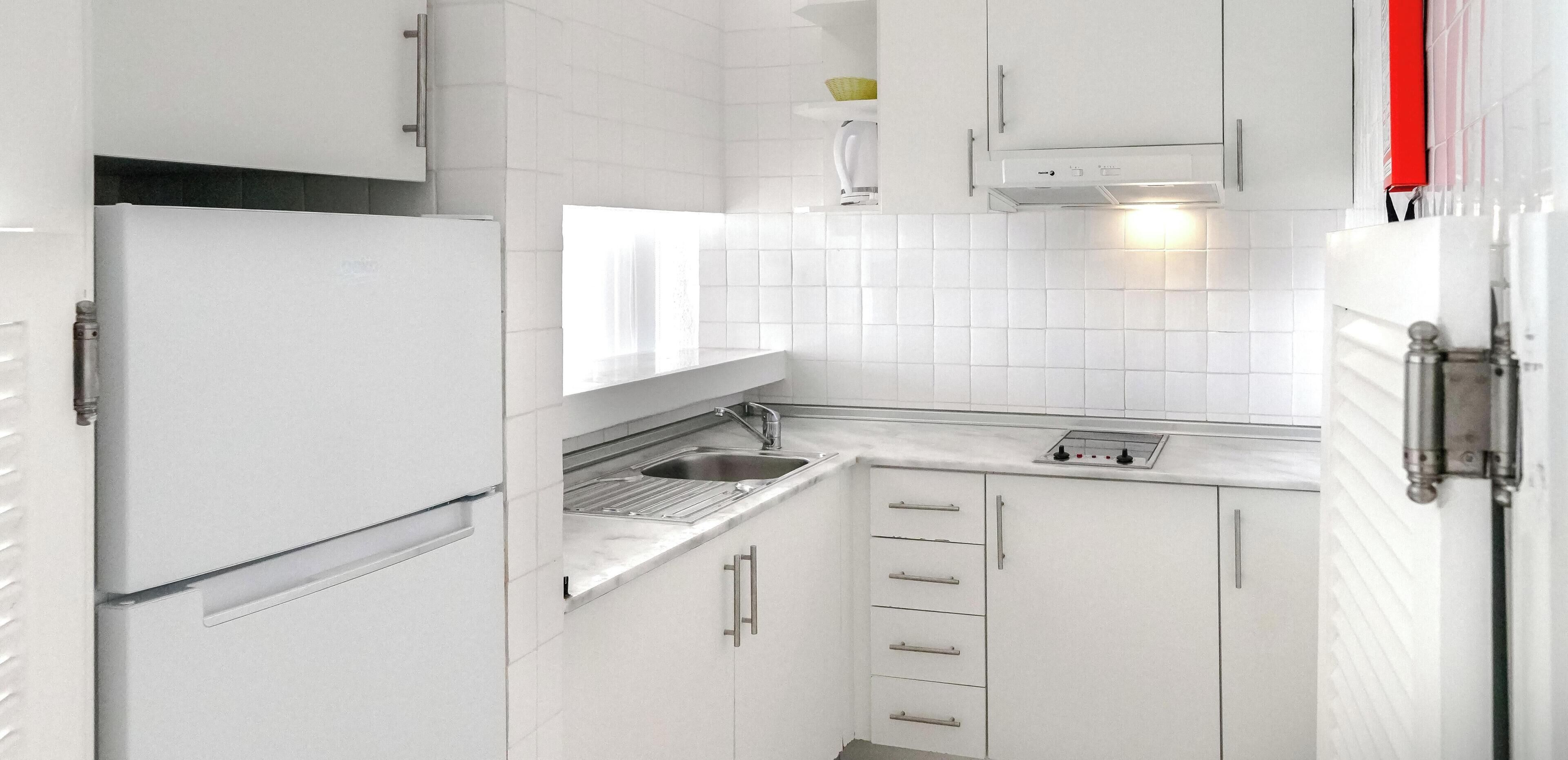 Une cuisine compacte avec des meubles blancs, un évier en acier inoxydable et un four encastré.