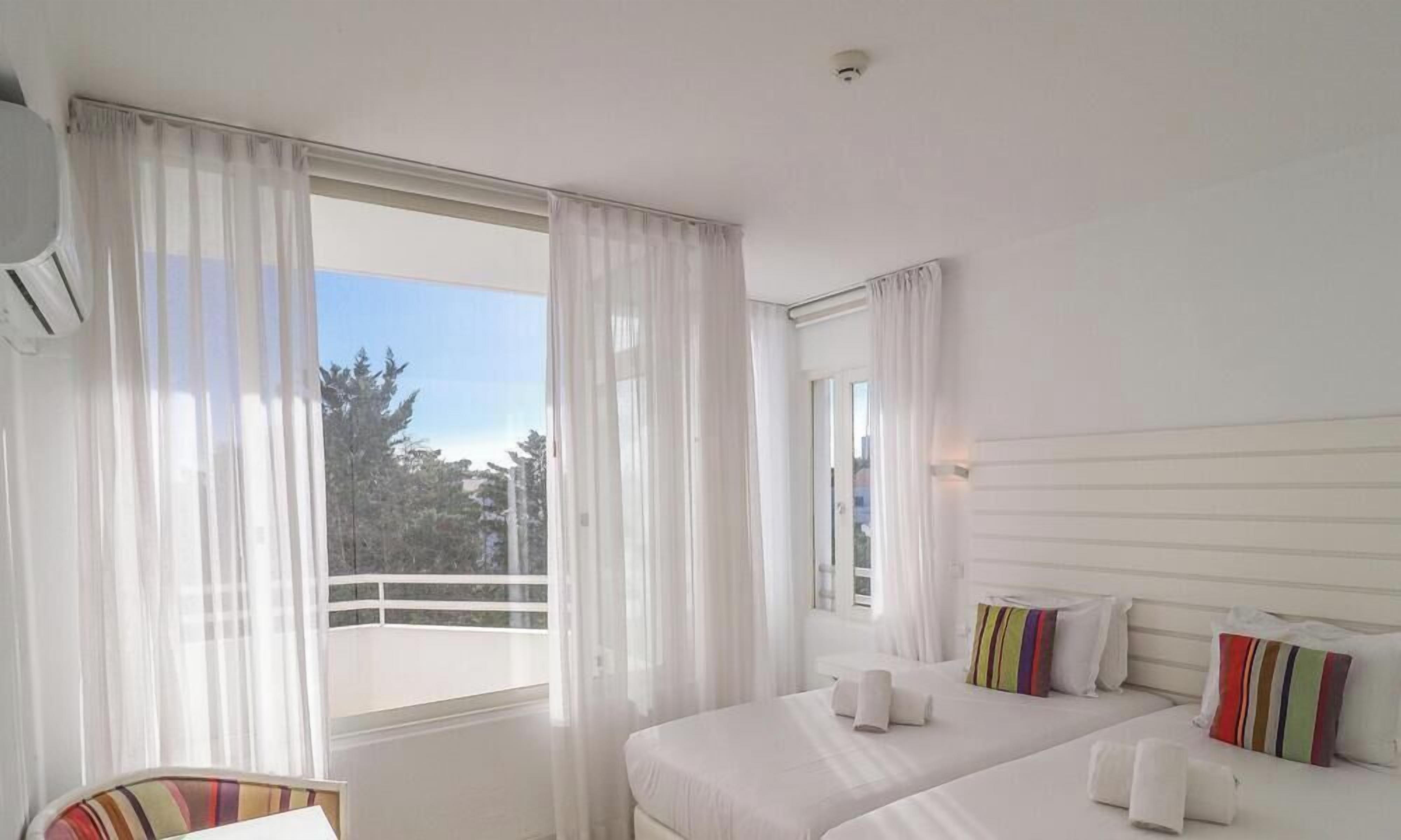 Ein Hotelzimmer mit Bett, Stuhl, einem Fenster mit Vorhängen und Blick auf Bäume.