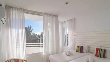 Ein Hotelzimmer mit Bett, Stuhl, einem Fenster mit Vorhängen und Blick auf Bäume.