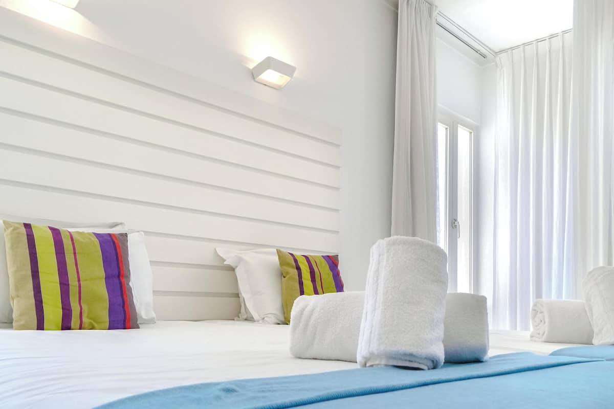 A hotel room with a bed, pillows, towels, a light fixture, and a window with curtains.