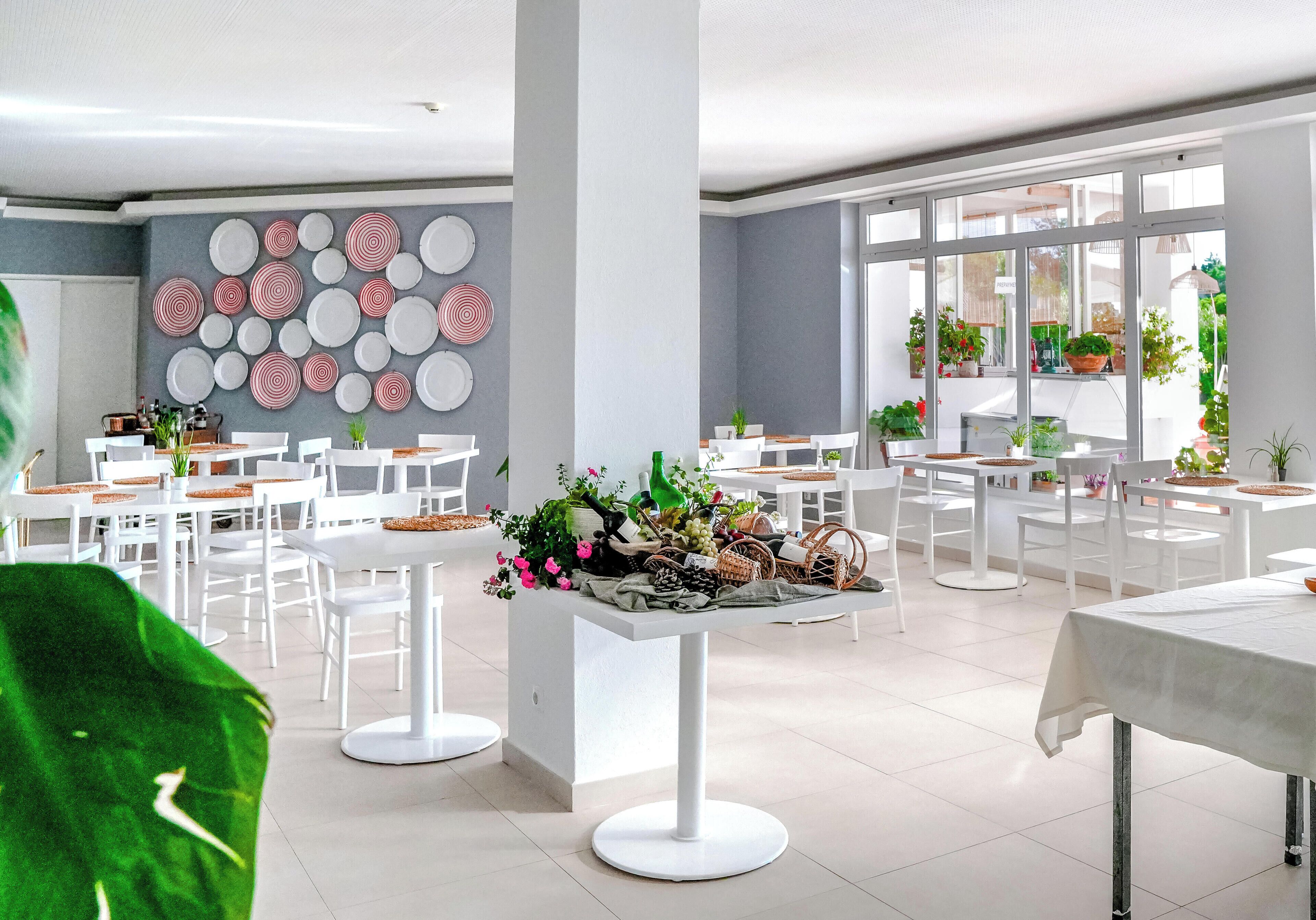 Un espace repas moderne avec des tables et des chaises blanches, un mur décoratif orné de motifs circulaires et des plantes en pot.
