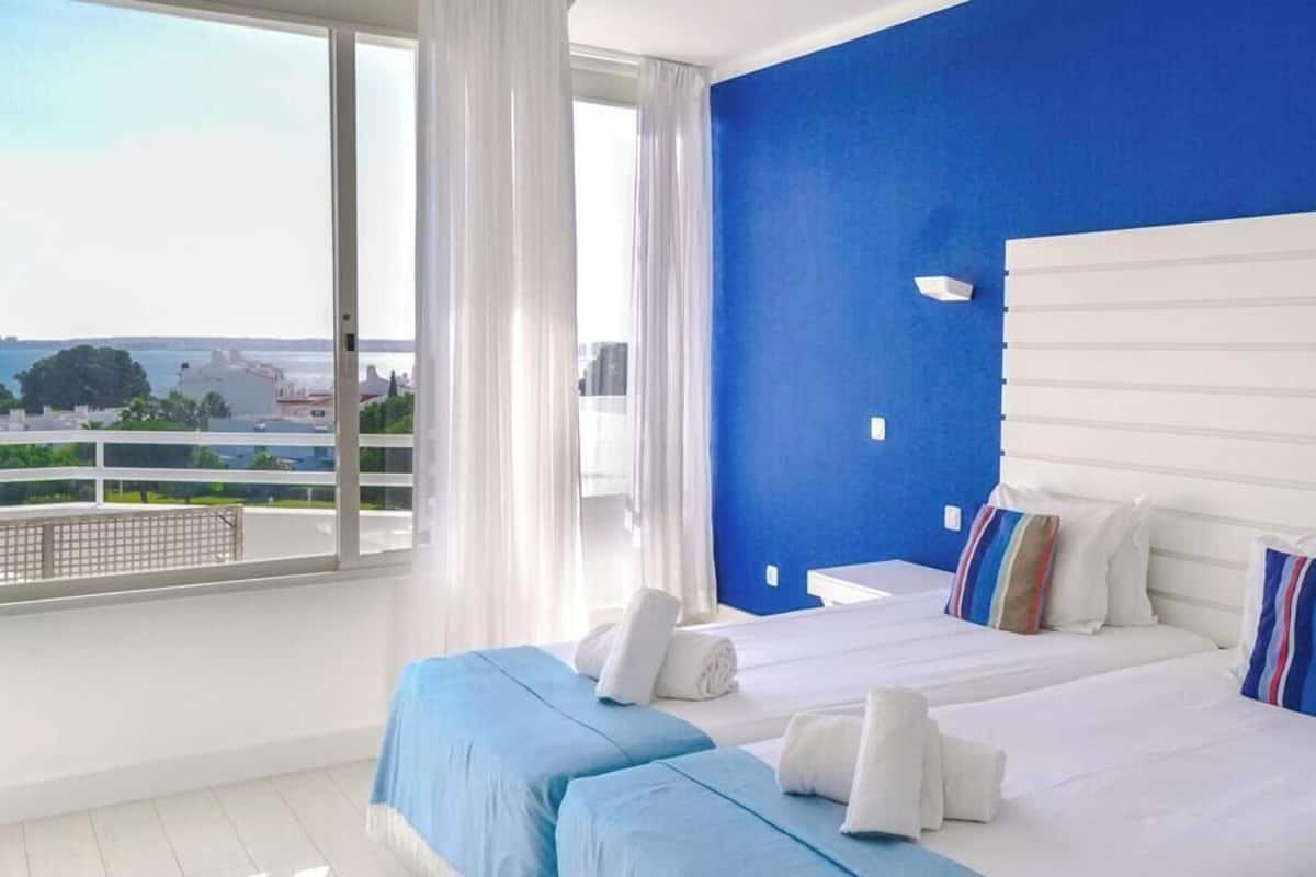 Une chambre dâhĂŽtel avec deux lits, une grande fenĂȘtre offrant une belle vue et un mur dâaccent bleu.