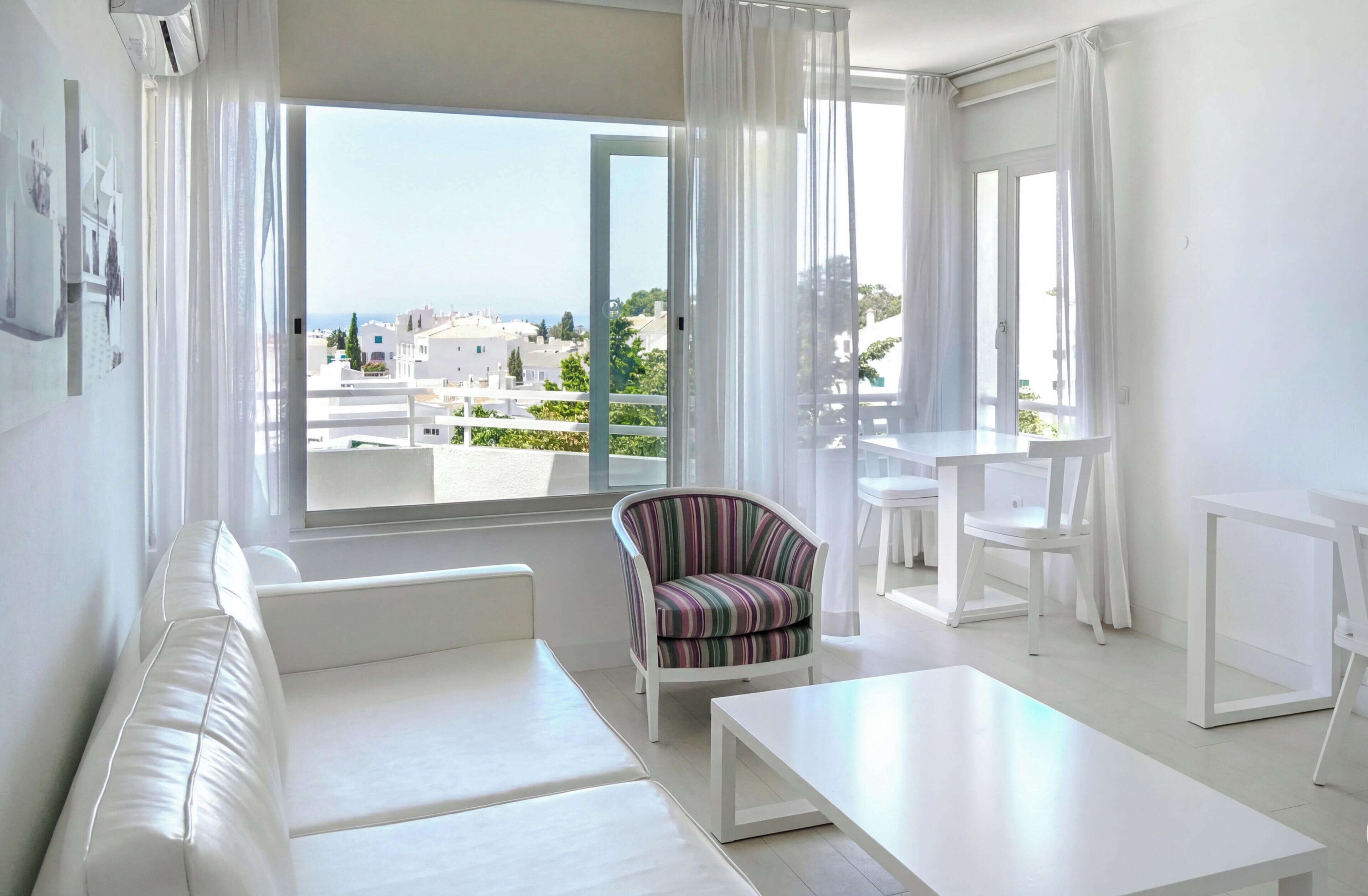 A modern living room with a white sofa, striped armchair, and a dining table.