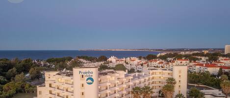 A coastal hotel with multiple floors, a prominent sign, and a view of the sea.