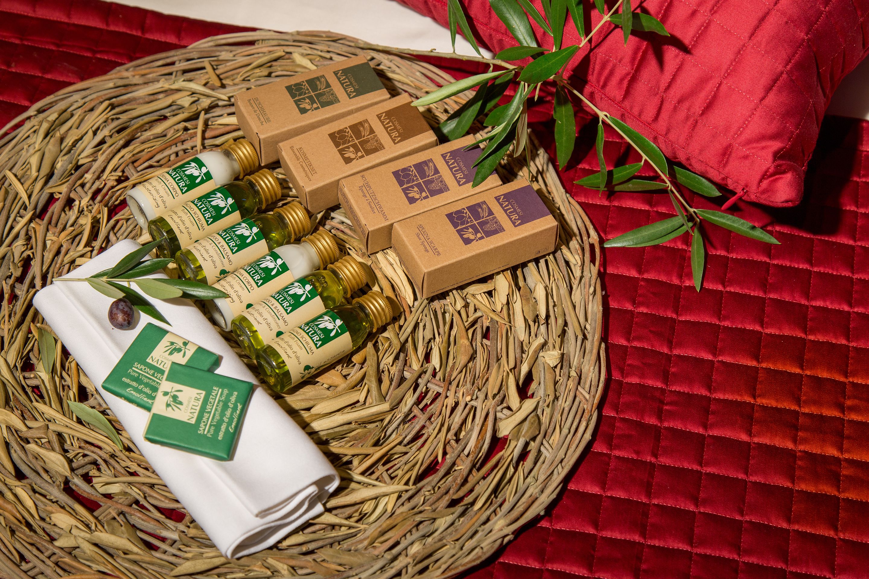 A wicker basket containing several bottles of natural essential oils and small cardboard boxes, placed on a red textured surface.