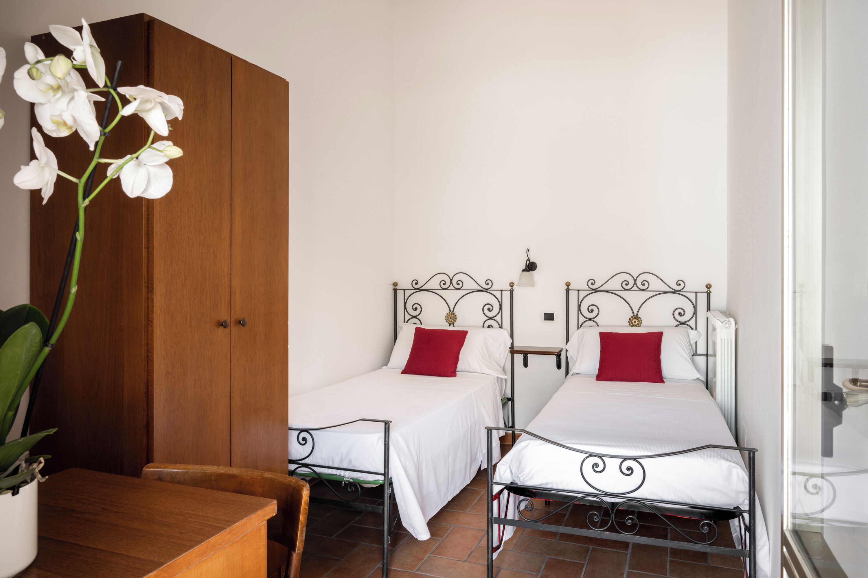 A room with two beds, a wooden wardrobe, a table, and a potted plant.