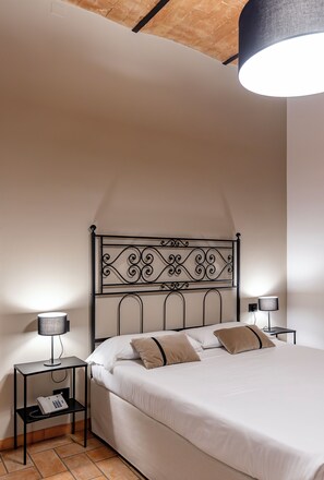 A bedroom with a metal headboard, a bed with white bedding, two bedside tables with lamps, and a telephone on one table. - Hotel San Marco (Gubbio)