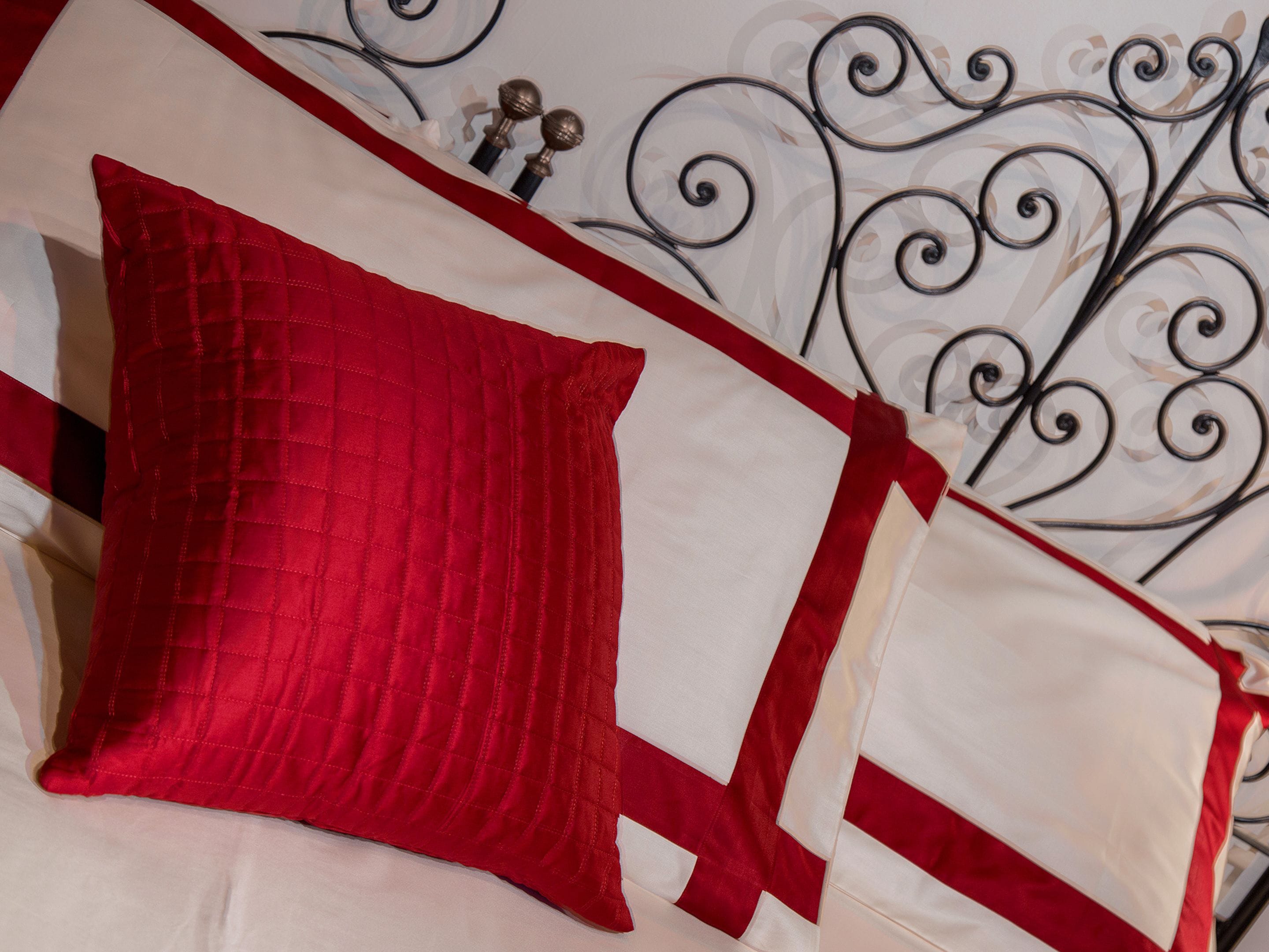 Un letto con cuscini biancorossi, una testata in metallo con motivo decorativo e una parete bianca sullo sfondo.