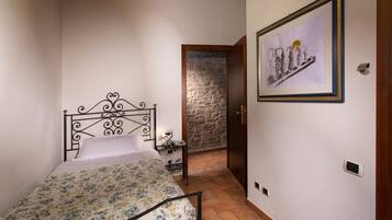 A bedroom with a bed, a nightstand, a framed picture, a stone wall, and a wooden door.