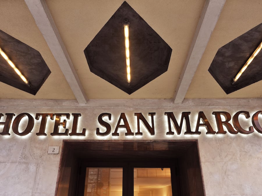 The entrance to HOTEL SAN MARCO with a prominent sign and three pendant lights above.