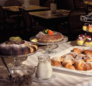 A dining table with various desserts, a milk jug, and a bowl of cereal. - Hotel San Marco (Gubbio)