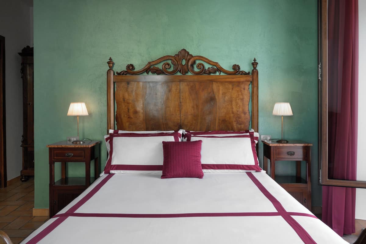 A neatly made bed with a wooden headboard, two bedside tables with lamps, and a green wall.