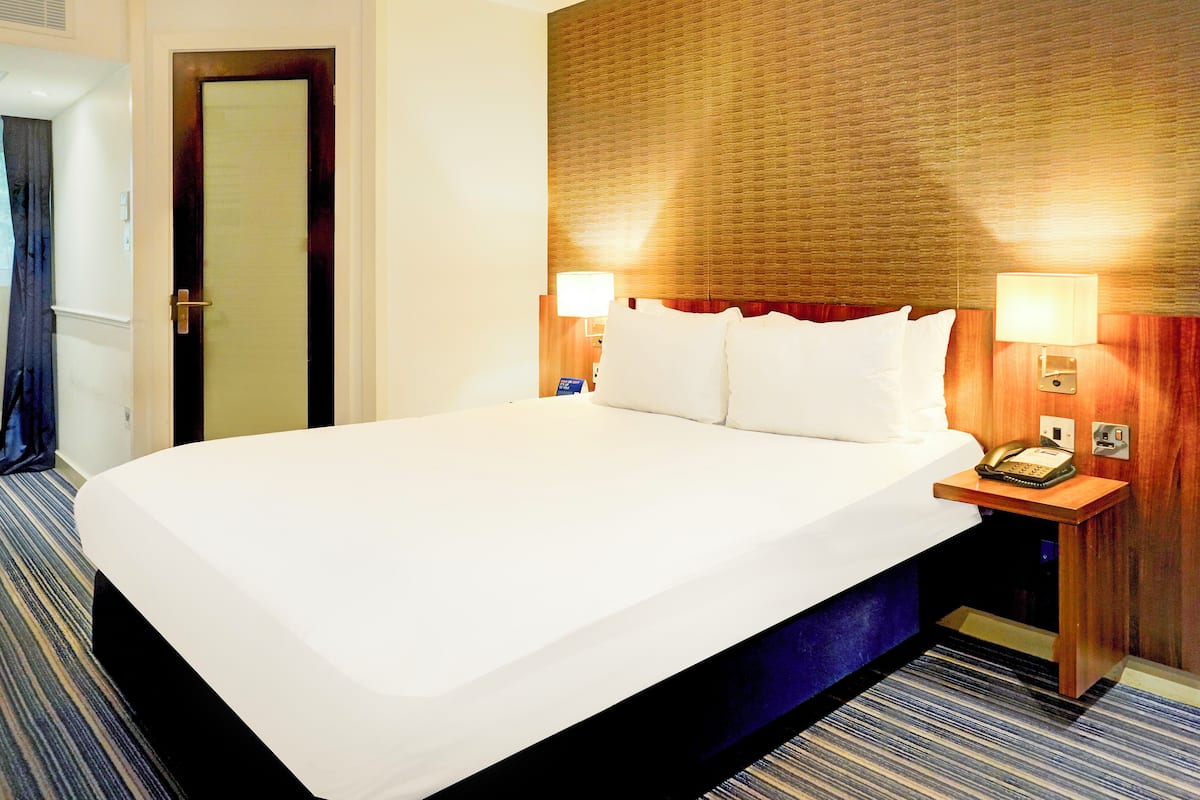 Habitación de hotel con una cama grande, dos lámparas de noche, una mesita de noche con teléfono y un cabecero de madera.