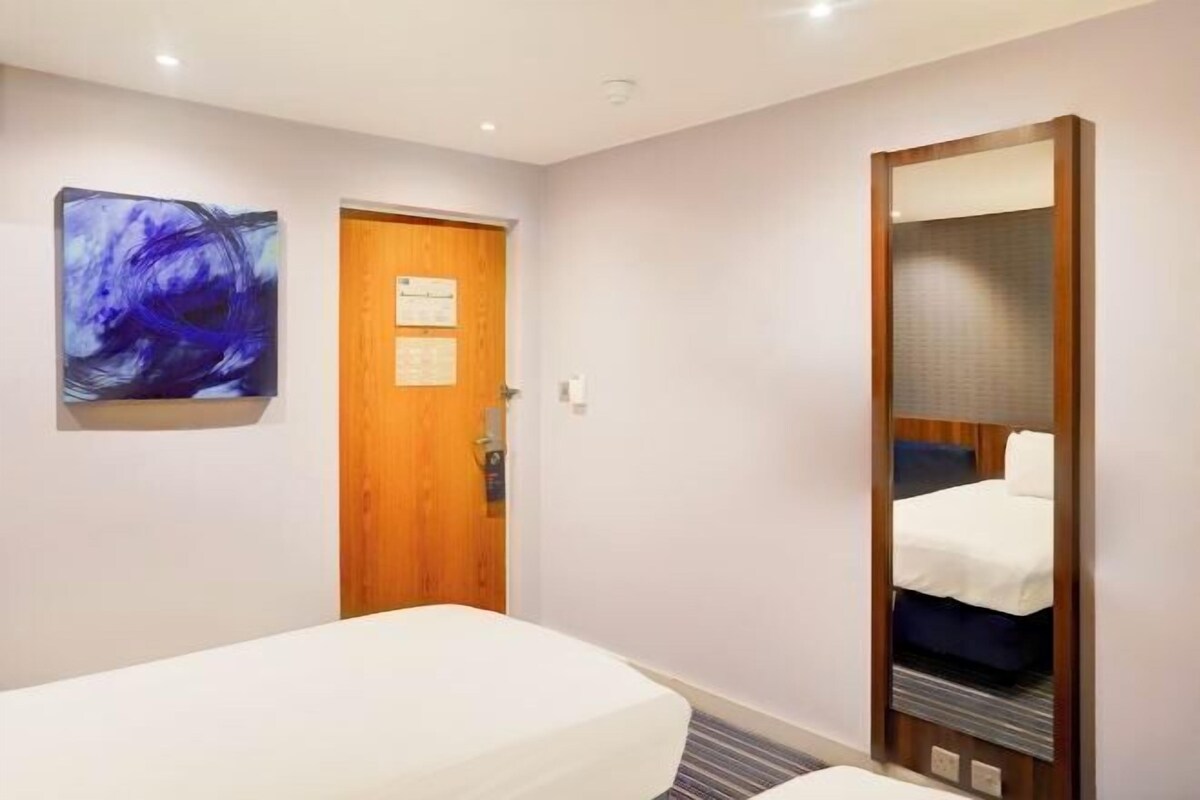 Une chambre d’hôtel avec un lit, une porte en bois, une œuvre d’art accrochée au mur et un miroir.