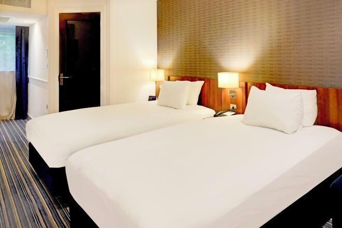 Une chambre d’hôtel avec deux lits, une tête de lit en bois et deux lampes de chevet.