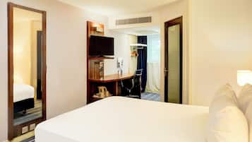 A hotel room with a large bed, a desk with a chair, a television, and a wardrobe.