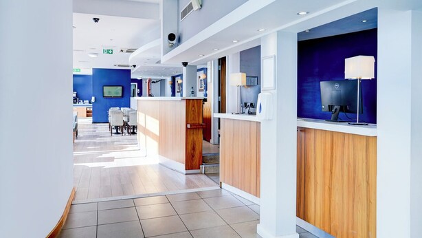 Een moderne hotellobby met een receptiebalie, een zithoek en een trap naar een andere verdieping.